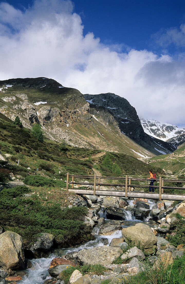 hiker on bridge across stream Suvrettabach, St. Moritz, Engadin, Switzerland