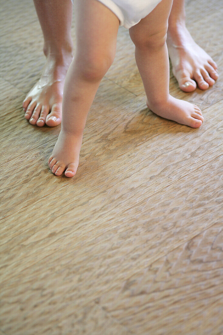 Baby und Vater stehen hintereinander, Nahaufnahme Füße