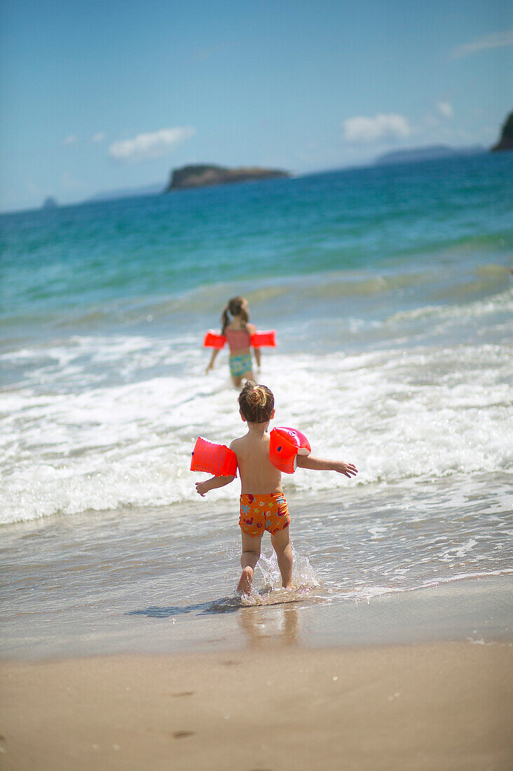 Kinder (5 und 2,5 Jährige mit Schwimmhilfen), baden in Wellen am Hahei Beach, bei Hahei, Ostküste, Coromandel Peninsula, Nordinsel, Neuseeland