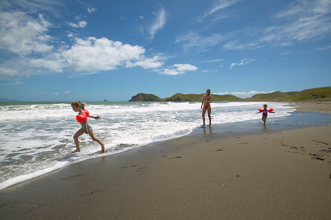 Children playing with their mother on the beach, Port Jackson on the northern tip of Coromandel Peninsula, North Island, New Zealand