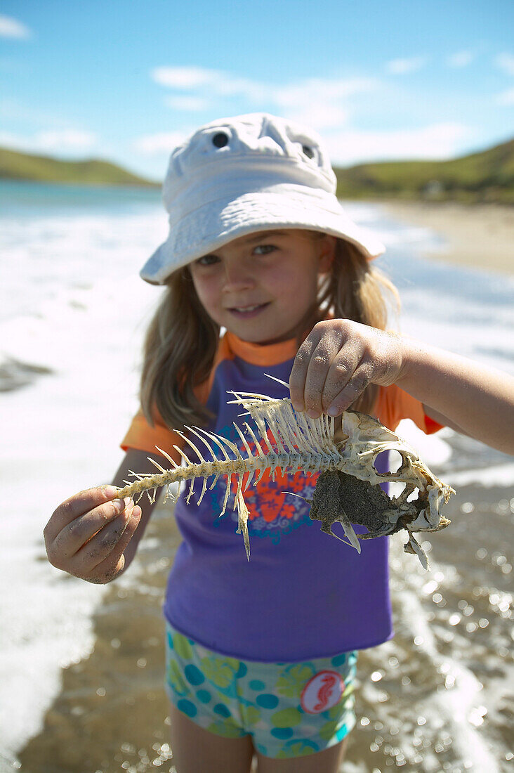 Mädchen mit Fischgräte, spielen am Strand, in Sonnenschutzkleidung, Strand von Port Jackson, Nordspitze der Coromandel Peninsula, Nordinsel, Neuseeland