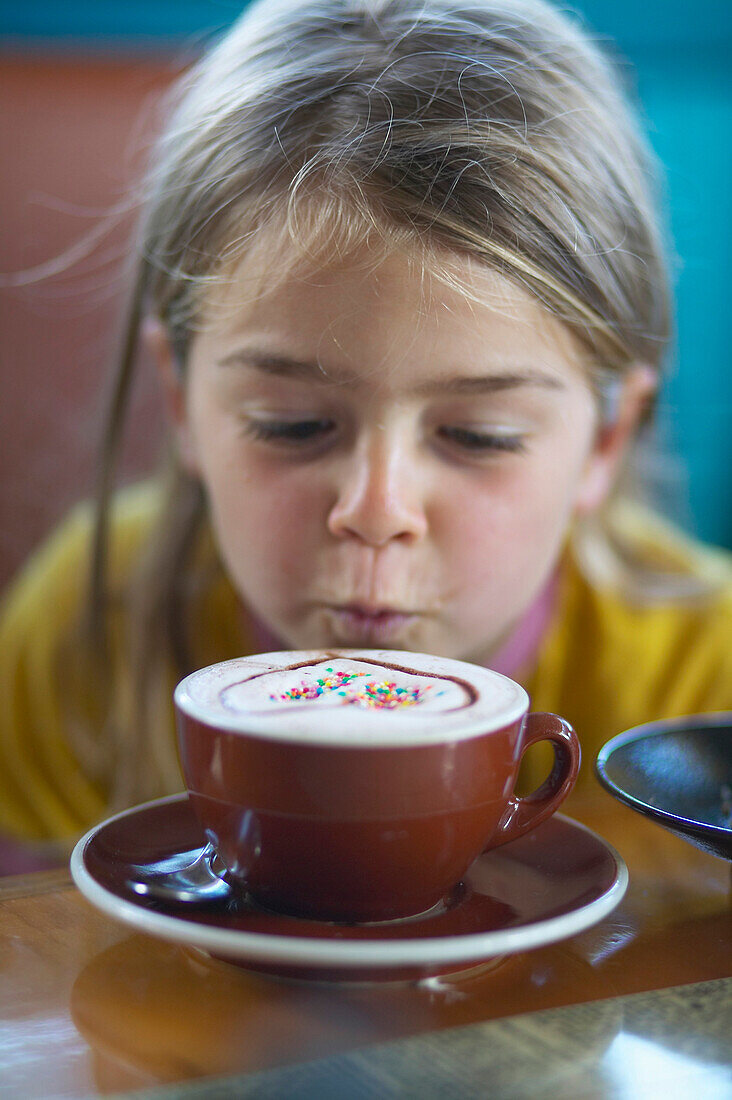 Mädchen (5 Jahre) blickt auf Tasse mit verziertem Cappuccino, Café, Bremen, Deutschland