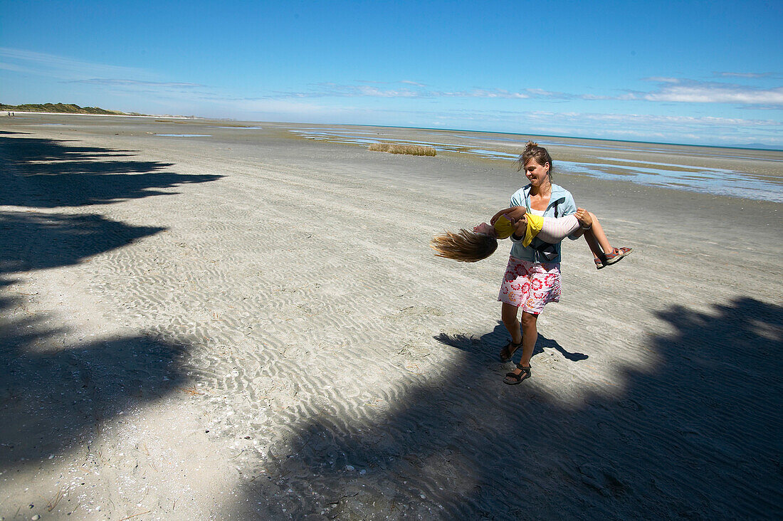 Spinning around, mother with daughter playing, beach at low tide, tidal flats, near Puponga, Golden Bay, northern coast of South Island, New Zealand