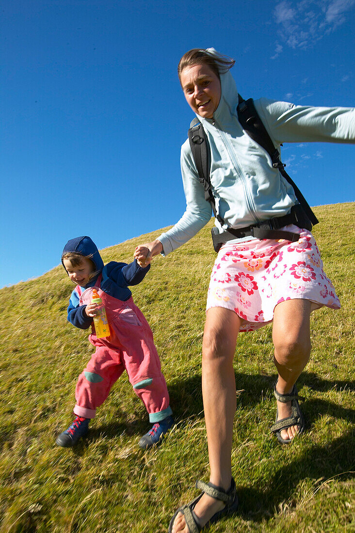 Mother and child running on farmland, sheep meadow, near Puponga, Golden Bay, northern coast of South Island, New Zealand