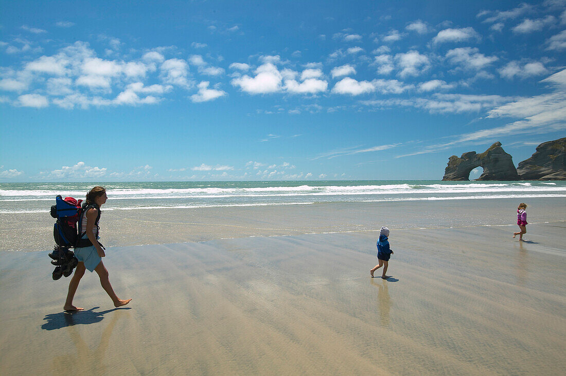 Family hiking on Wharariki Beach, low tide, near Puponga, northwestern coast of South Island, New Zealand