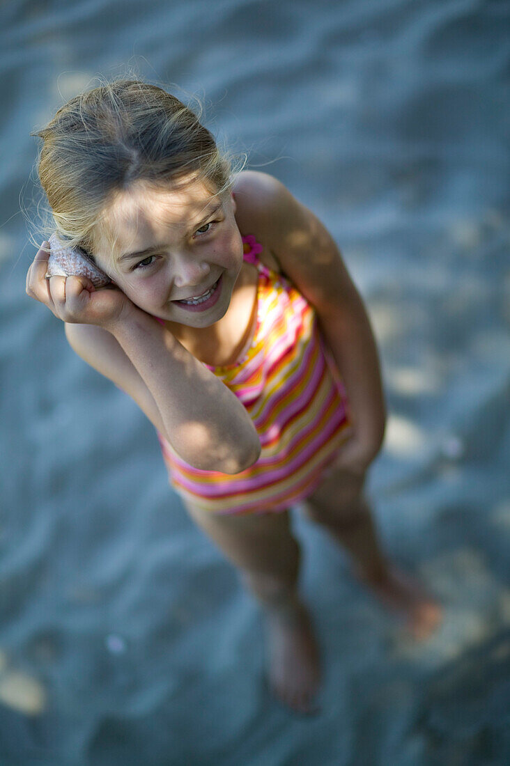 Girl listening to seashell, found at Pakawau beach, Golden Bay, northern coast of South Island, New Zealand