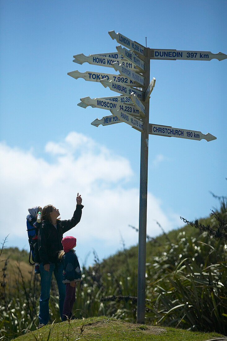 Mother with two kids at signpost, showing overseas cities, Cape Foulwind, northern Westcoast, South Island, New Zealand