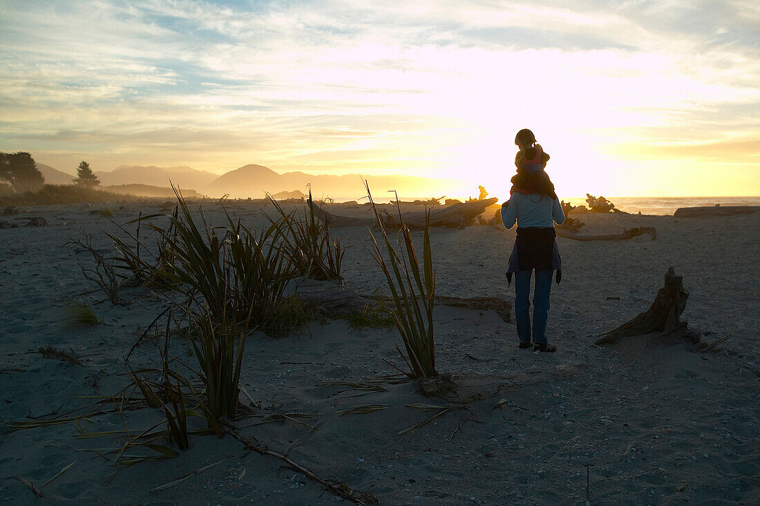 Wanderung zwischen Treibholz, Muttert rägt Kind auf Schultern, Sonnenuntergang, Strand bei Haast, Westküste, Südinsel, Neuseland