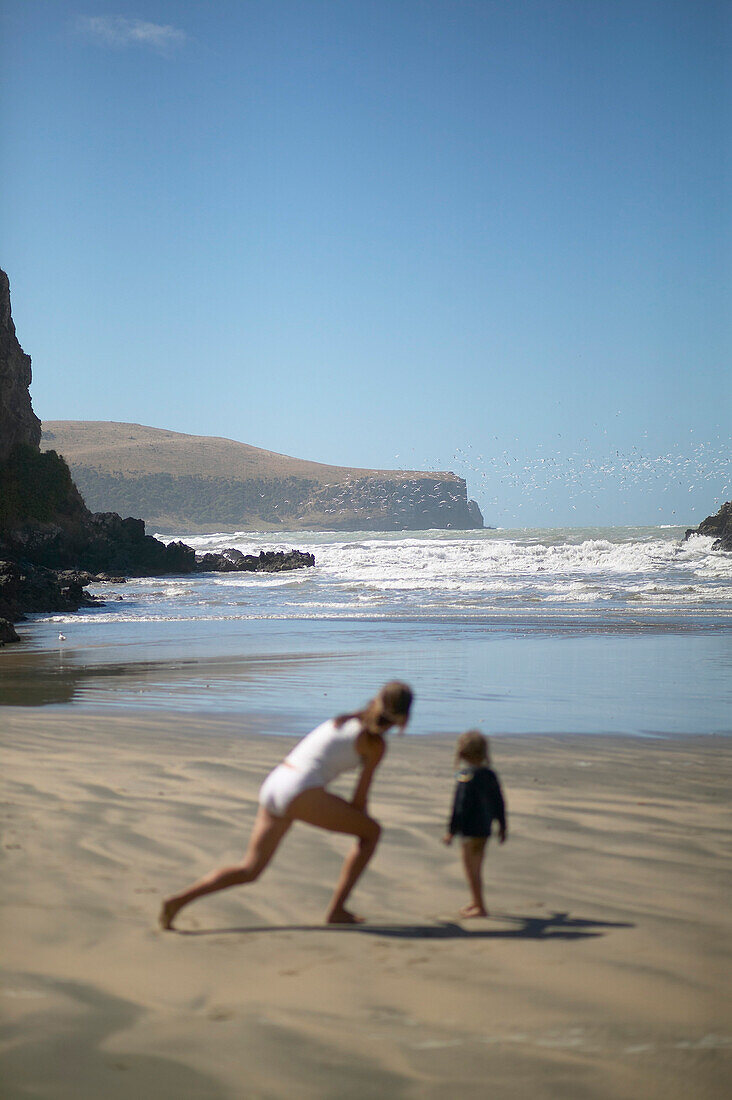 Mother and child playing at the beach of Little Okains Bay at low tide, Okains Bay, Bank`s Peninsula, east coast, South Island, New Zealand