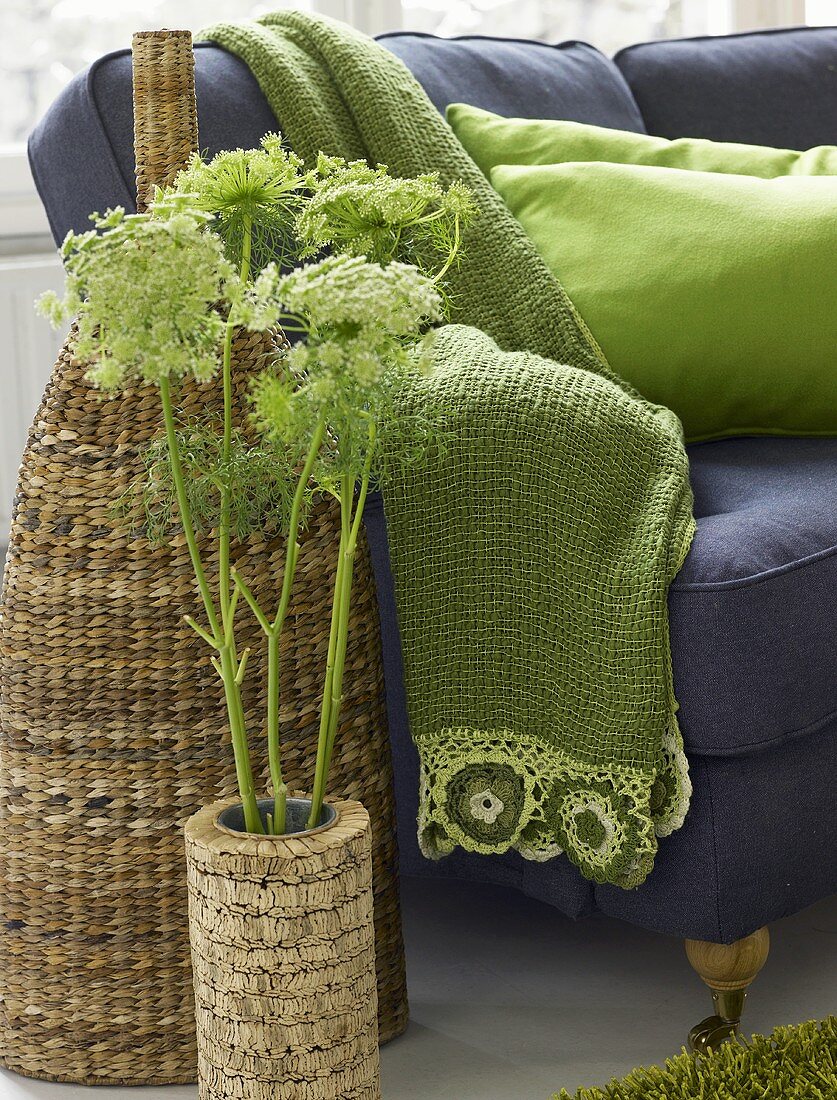 A cork plant pot in front of a rattan vase and green blanket on a sofa