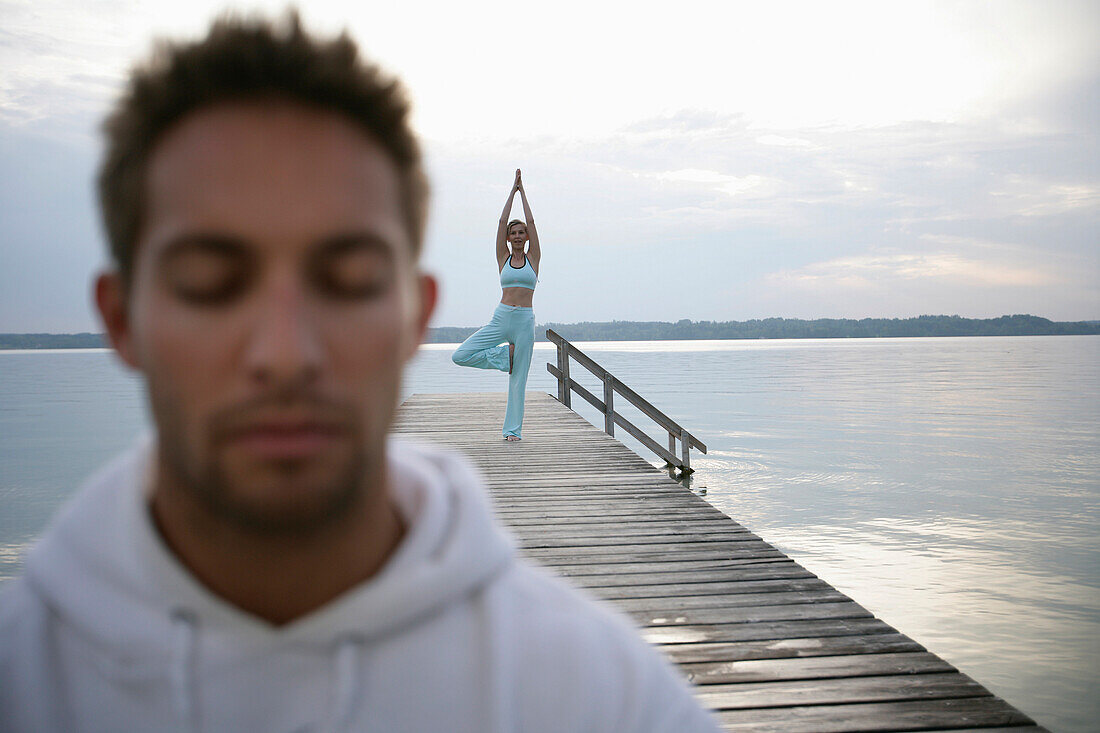 Mann mit geschlossenen Augen, Frau beim Yoga auf Steg am Starnberger See, Münsing, Bayern, Deutschland, MR