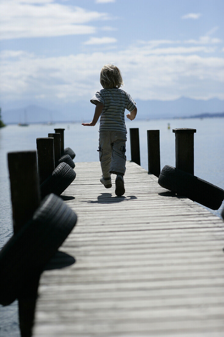 Boy walking over jetty, Possenhofen, Lake Starnberg, Bavaria, Germany