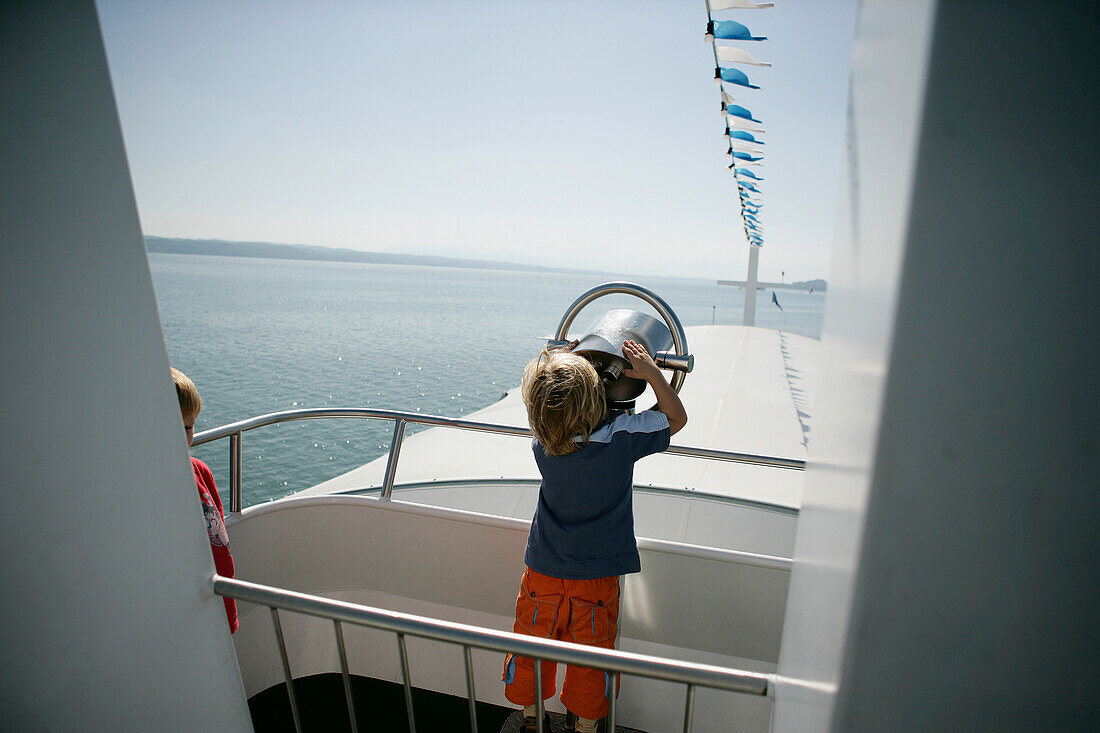 Junge blickt durch ein Fernglas auf einem Boot, Starnberger See, Bayern, Deutschland, MR
