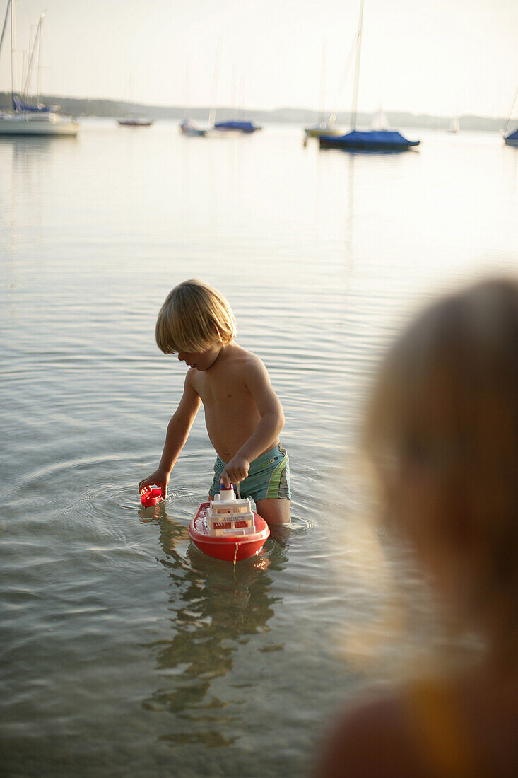 Boy playing with toy boat in Lake Woerthsee, Bavaria, Germany, MR