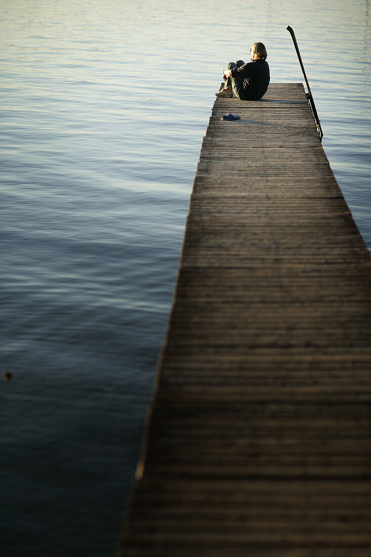 Woman sitting on far end of jetty, Steg, Lake Woerthsee, Bavaria, Germany