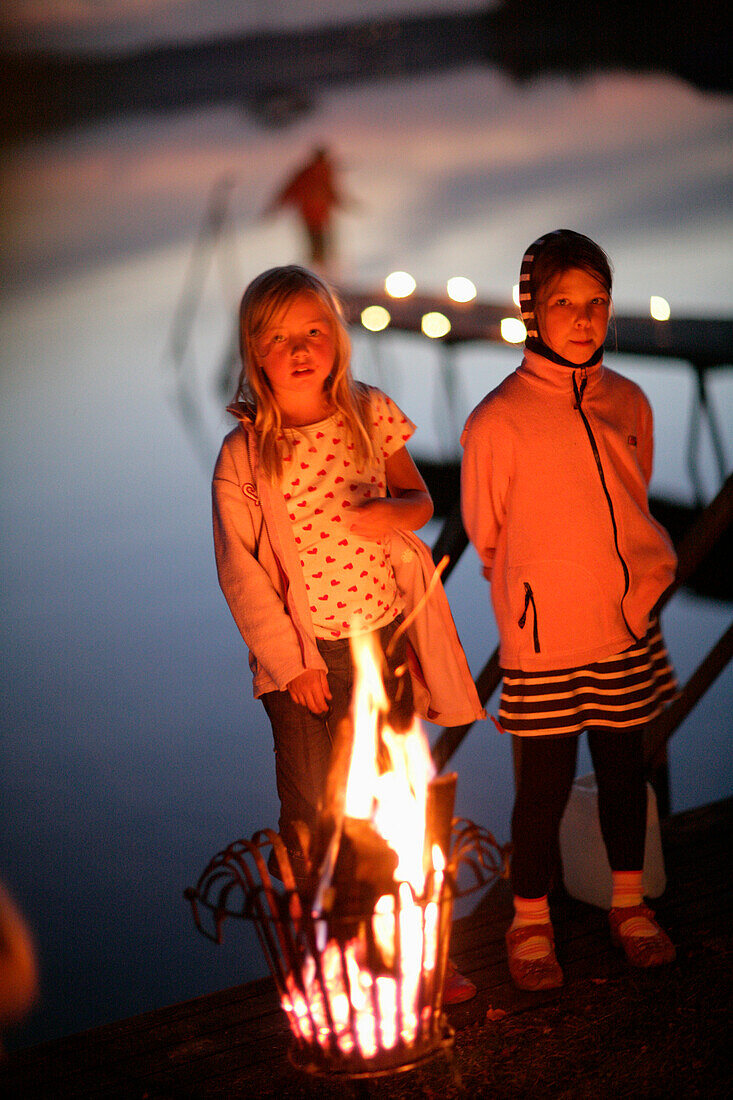 Zwei Mädchen am Seeufer an einem Feuerkorb, Wörthsee, Walchstadt, Bayern, Deutschland, MR