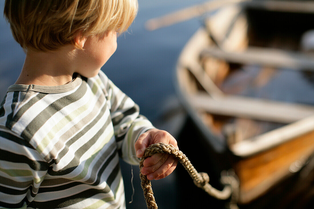 Boy (3-4 years) holding rope of a rowboat, Lake Staffelsee, Upper Bavaria, Bavaria, Germany, MR