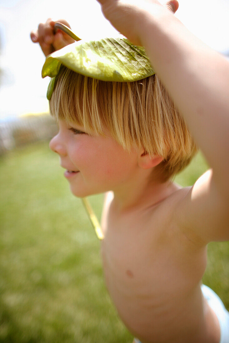 Boy (4-5 years) using a water lily leave as hat, Lake Staffelsee, Upper Bavaria, Bavaria, Germany