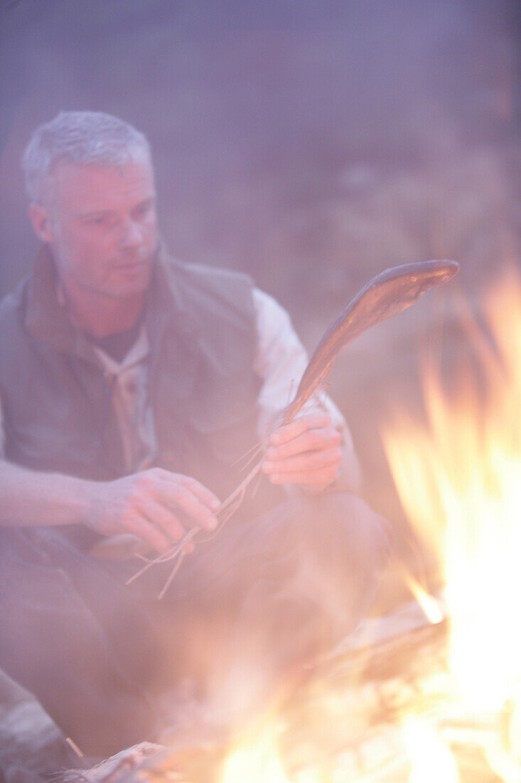 Mann bereitet Fisch am Lagerfeuer zu, Bayern, Deutschland, MR