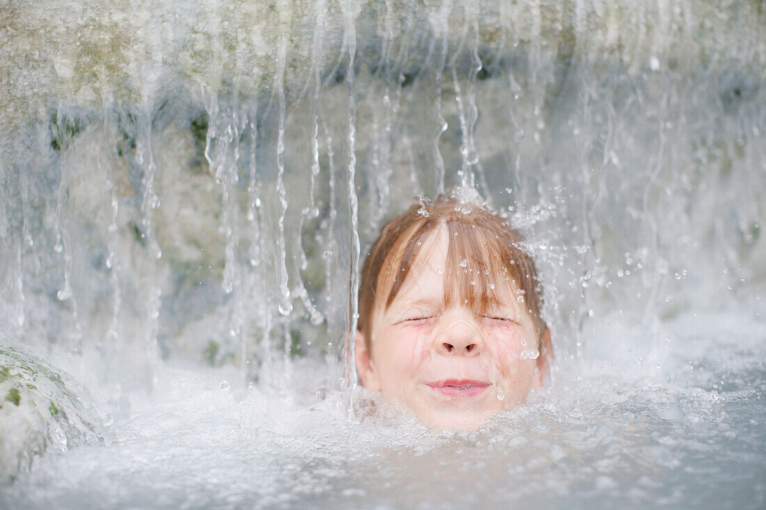 Junge (3-4 Jahre) badet unter einem Wasserfall, Bayern, Deutschland, MR