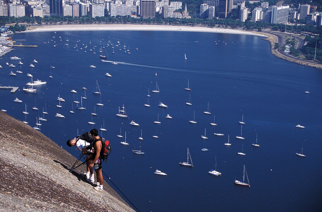 Two young men climbing on Sugarloaf Mountain Pao de Acucar, Rio de Janeiro, Rio de Janeiro State, Brazil