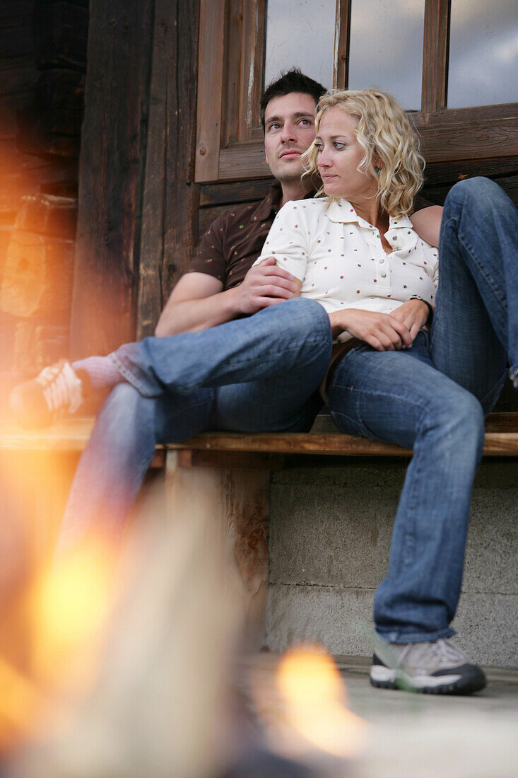 Young couple sitting on a bench near campfire, Heiligenblut, Hohe Tauern National Park, Carinthia, Austria