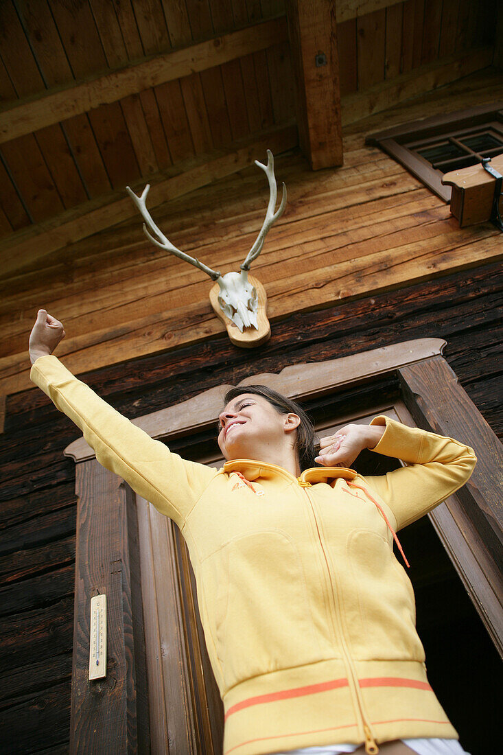 Woman yawning and stretching in front of alp lodge, Heiligenblut, Hohe Tauern National Park, Carinthia, Austria