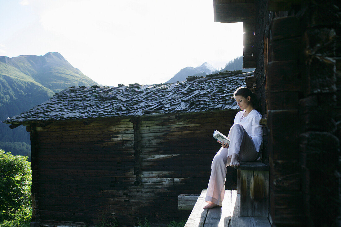 Woman reading a book in front of alp lodge, Heiligenblut, Hohe Tauern National Park, Carinthia, Austria