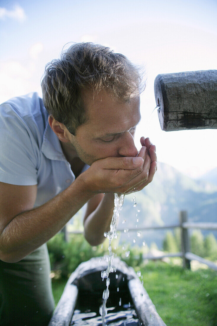 Mann trinkt Wasser von einem Brunnen, Heiligenblut, Natinalpark Hohe Tauern, Kärnten, Österreich