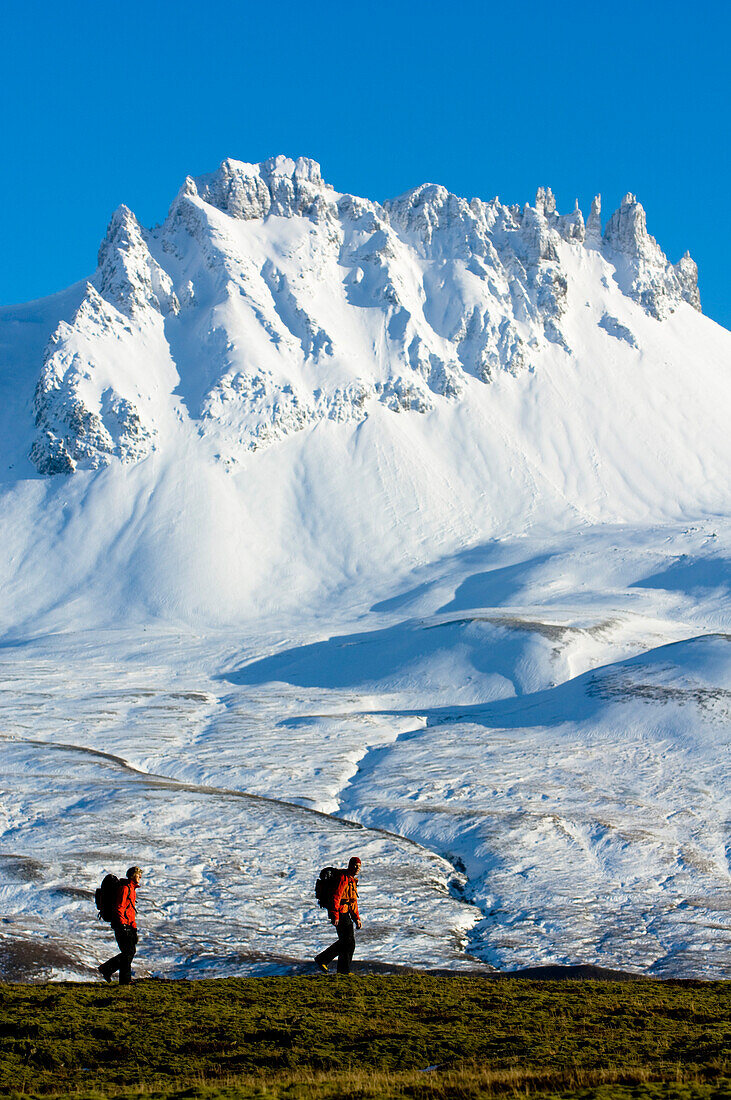 Two hikers passing snow covered mountain range, Iceland