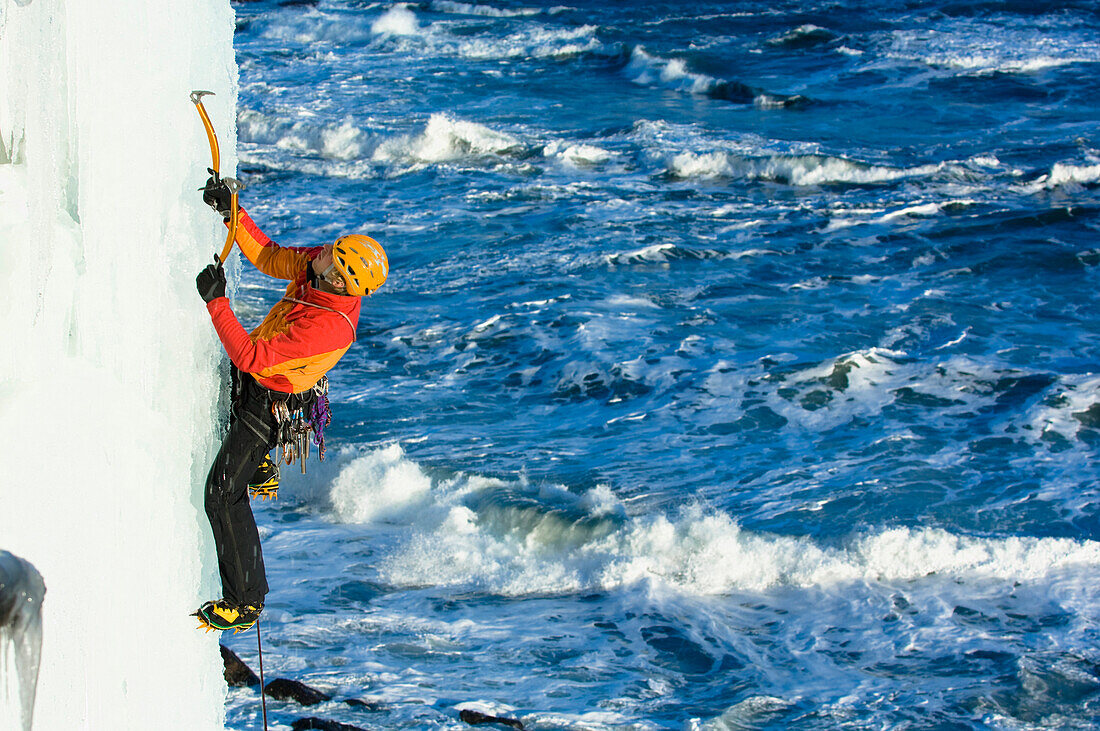 Ice climber in frozen waterfall above ocean, Kaldakinn, Iceland