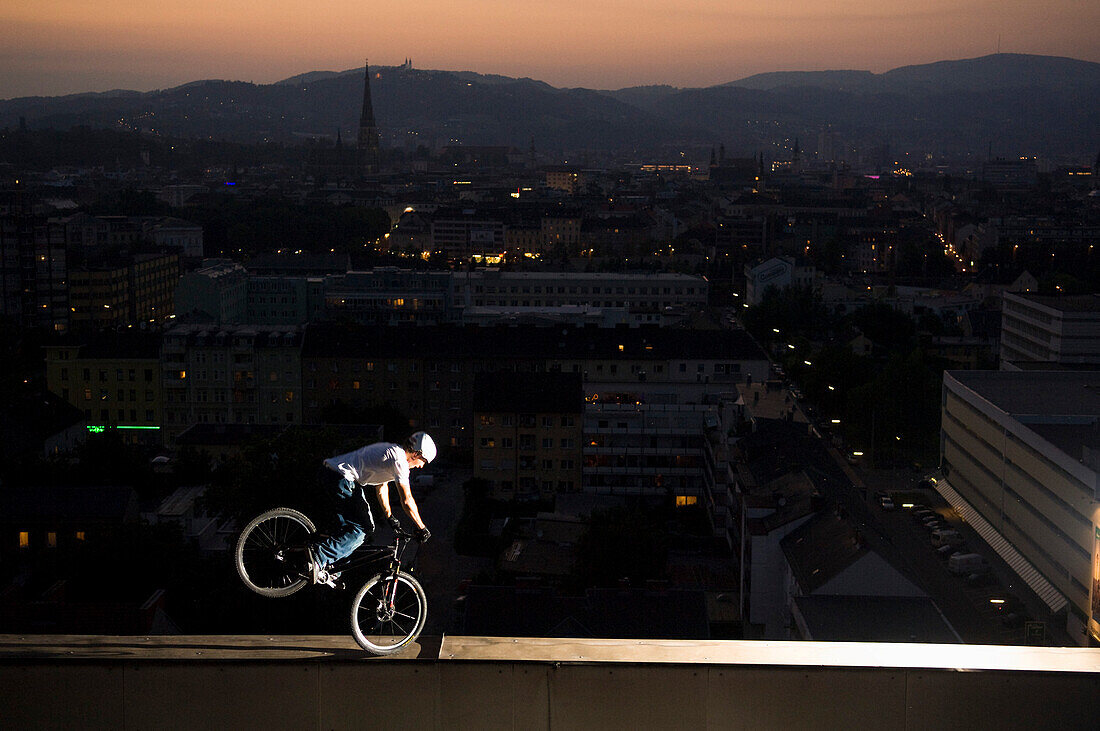 Trialbiker balanciert auf Kante von einem Hochhaus, Linz, Oberösterreich, Österreich