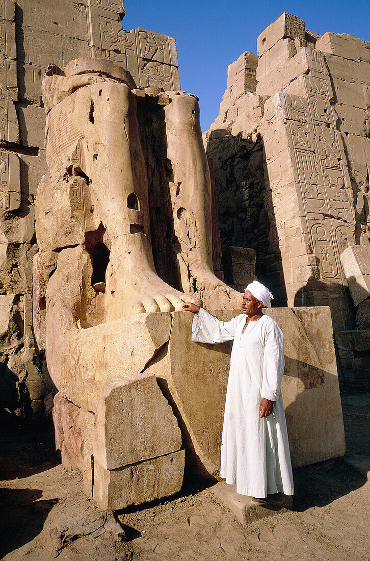 Warden by the remaining legs of a pharaon statue. Karnak temple. Luxor. Egypt