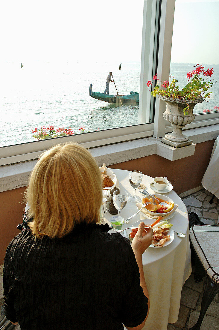 Woman having breakfast on the Hotel Cipriani Terrace, gondola passing by at back. Giudecca island. Venice. Venetia. Italy