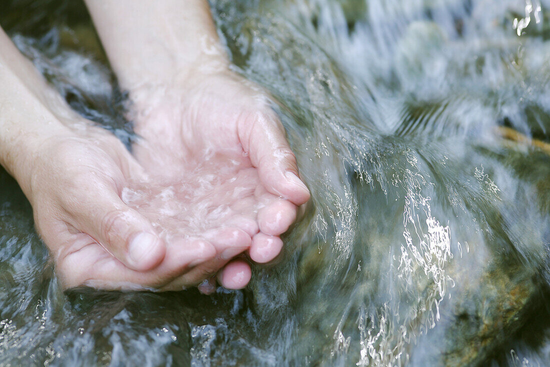 Hände im fließendem Wasser von einem Bach, Steiermark, Österreich