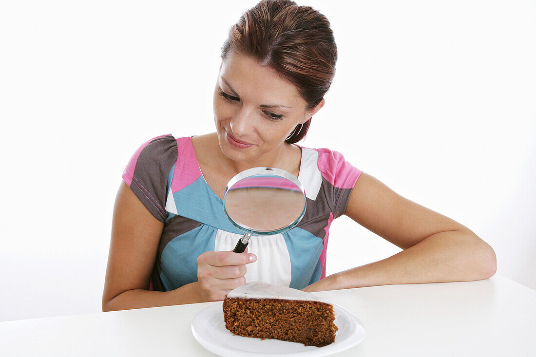 Woman observing chocolate cake through magnifying glass, Styria, Austria