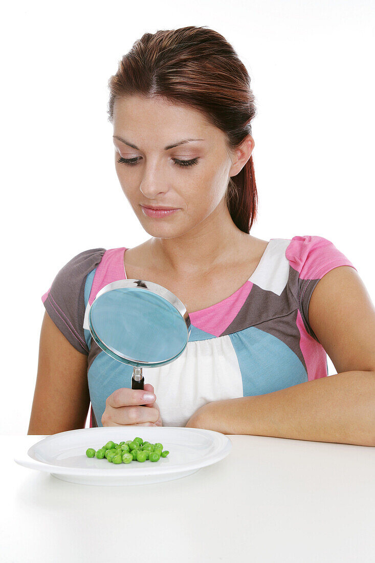 Woman observing peas on a plate through magnifying glass, Styria, Austria