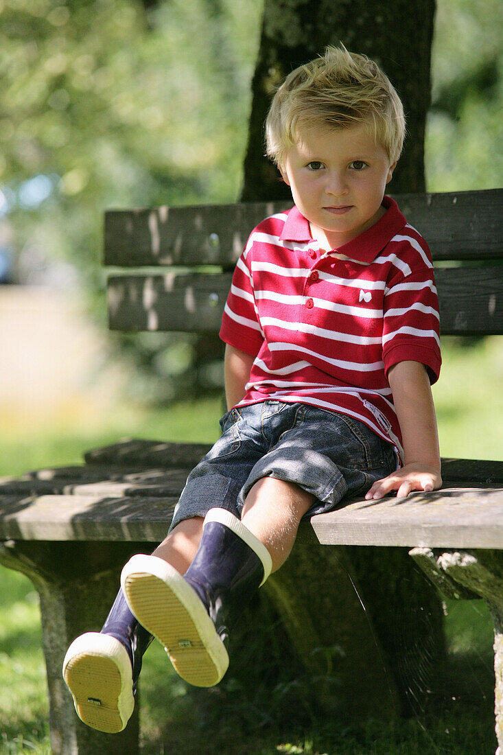 Junge (4-5 Jahre) sitzt auf einer Gartenbank, Steiermark, Österreich