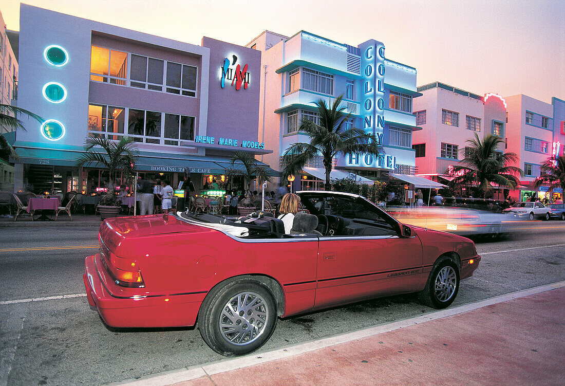 Red Convertible on Ocean Drive at dusk, Art deco hotels behind. Miami Beach. Florida. USA