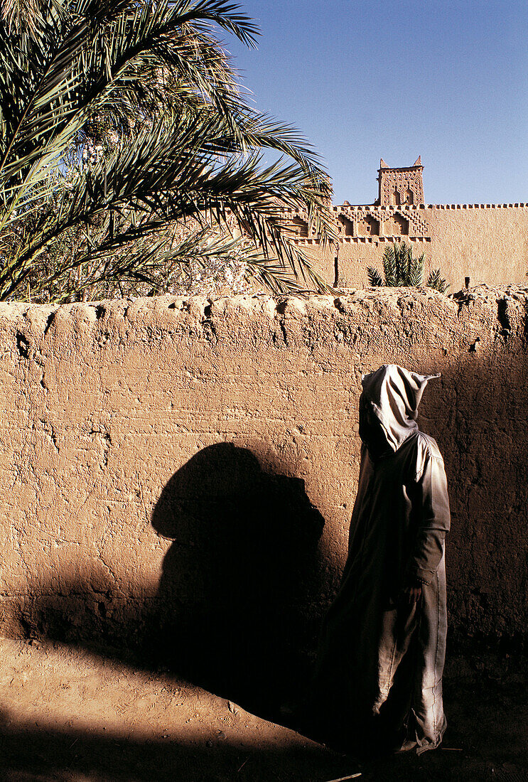 Man wearing a Djellabah against an adobe wall. Skoura oasis. Morocco