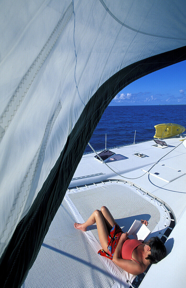 Cruising on a sailboat, woman reading on deck. British Virgin Islands