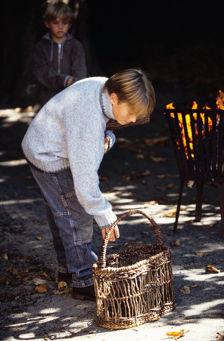 Young boy standing next to a basket next to an open fire