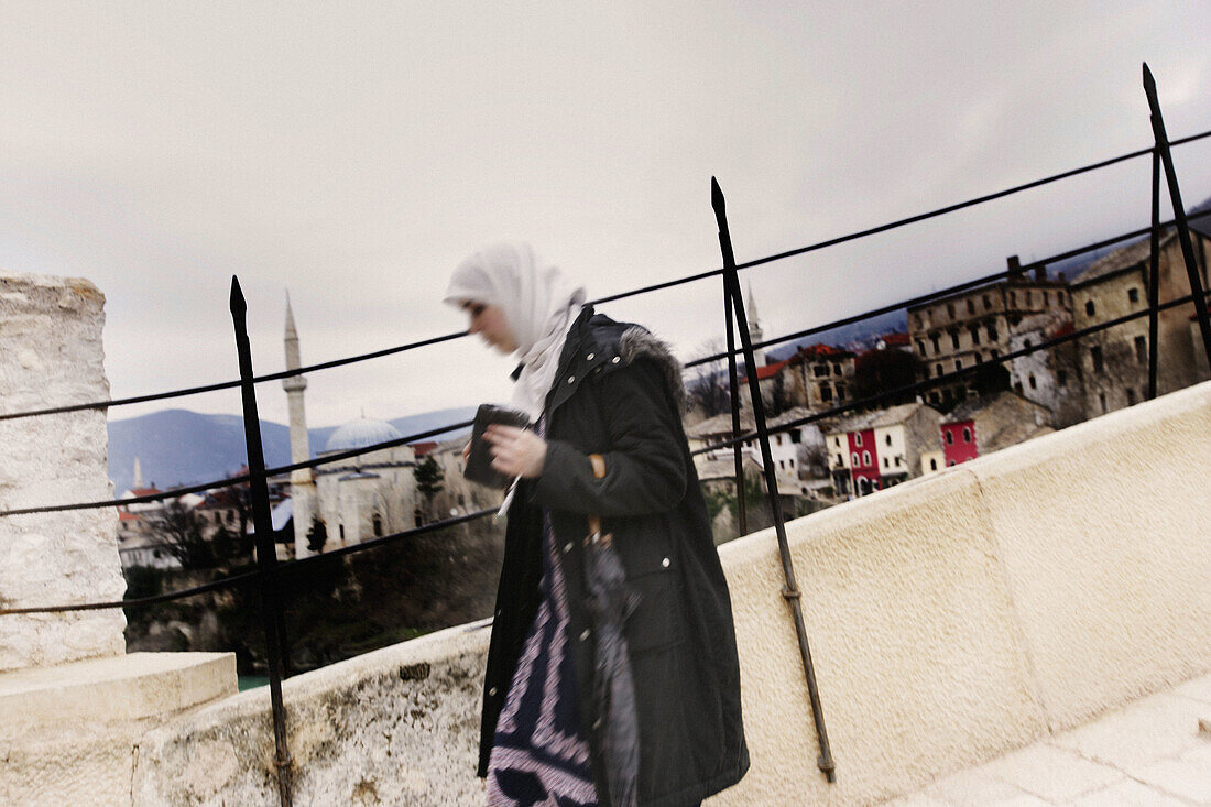 Young Muslim woman crossing the Old Bridge on the Neretva river, Mostar. Bosnia and Herzegovina