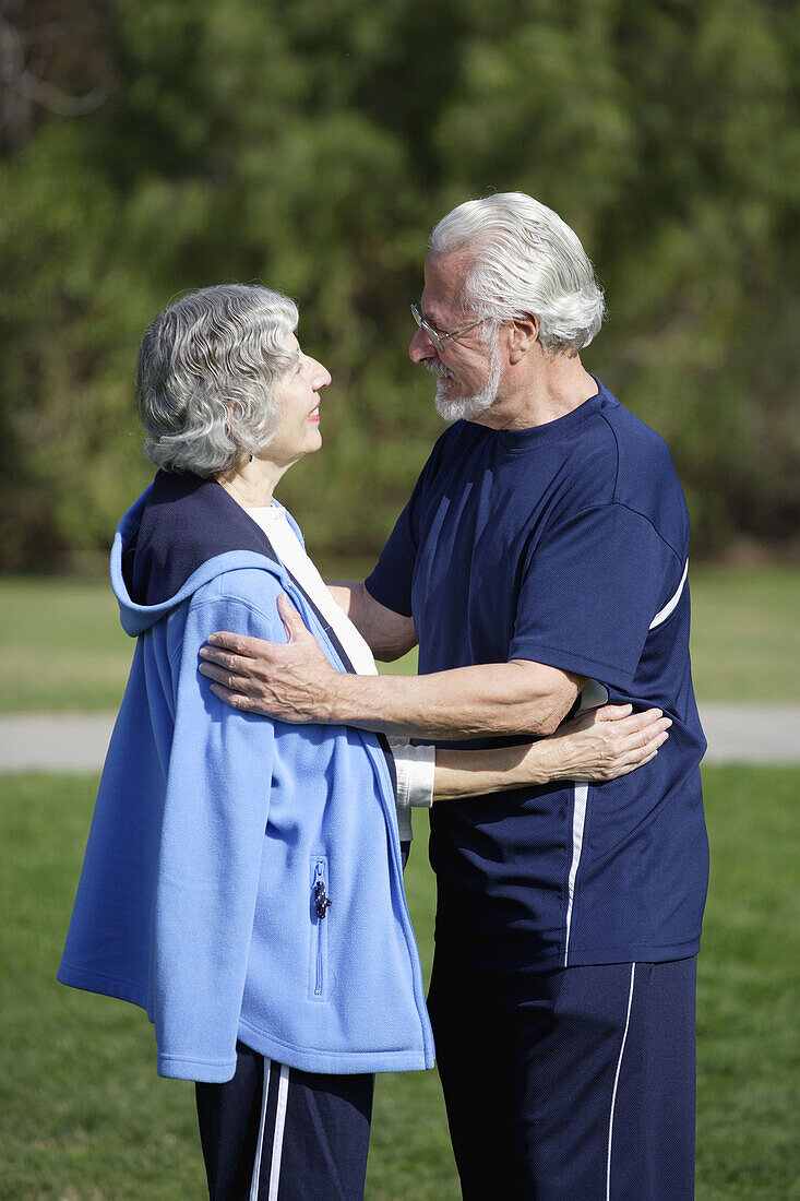 Active senior couple in exercise clothes embrace each other in an outdoor park.