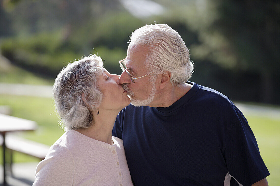 Portrait of active senior couple in exercise clothes kissing each other in an outdoor park.