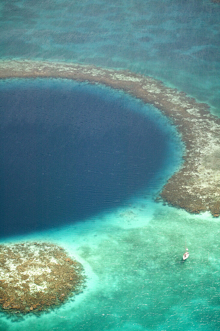 Aerial view of Blue Hole, sailboat anchored nearby, Lighthouse Atoll, Belize