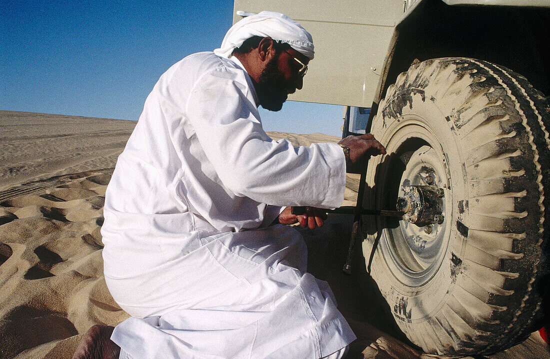Bedouin wearing the traditional local costume changing tyre in the Great Sand Sea, Lybian desert, Siwa Oasis. Egypt