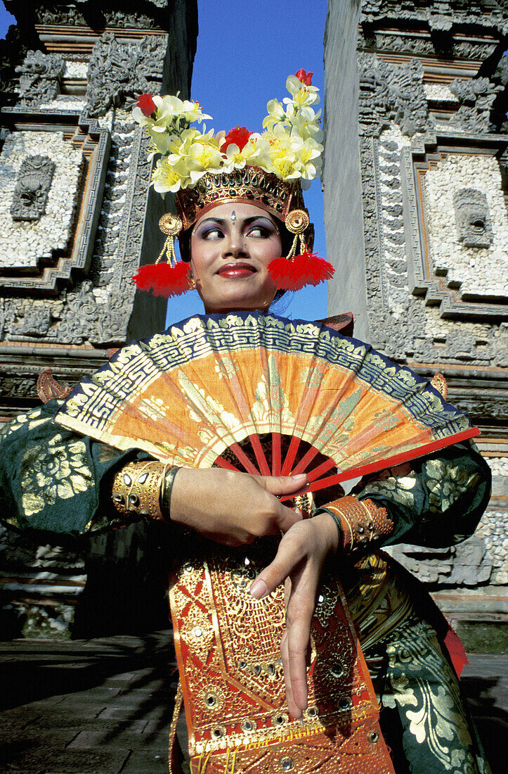 Young female dancer performing Legong Kraton (Palace Dance) by a Temple gate. Bali Island. Indonesia