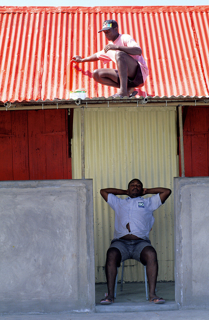 Landlord in shadow while a man is reparing the roof. Rodrigues Island. Mauritius