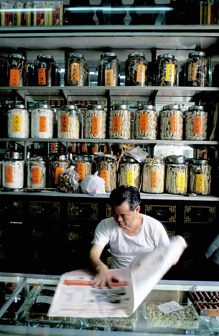 Herbalist reading newspaper in his shop. Macau. China